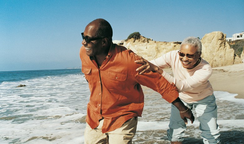 An older couple laughing together while walking along the beach